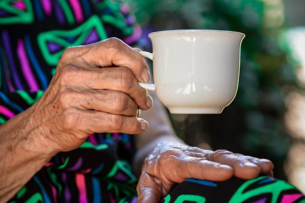 A hand holding a cup of tea in a brightly coloured dress